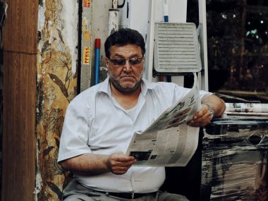 man in white polo shirt reading newspaper